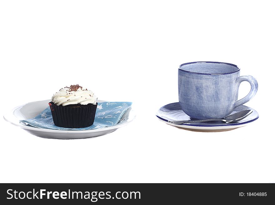 Pottery cup and saucer alongside schocolate cupcake with cream icing. Pottery cup and saucer alongside schocolate cupcake with cream icing