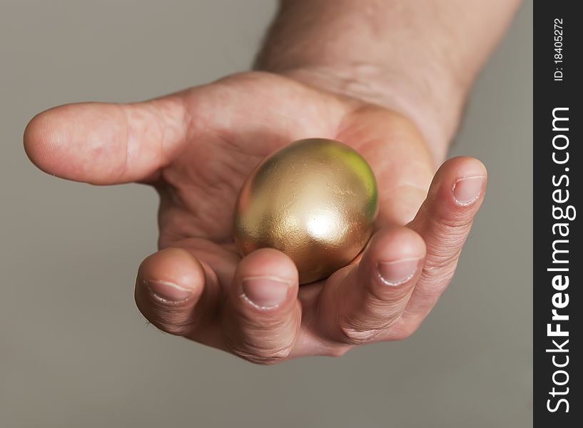 The man holds in a hand gold egg as a symbol of financial success. The man holds in a hand gold egg as a symbol of financial success