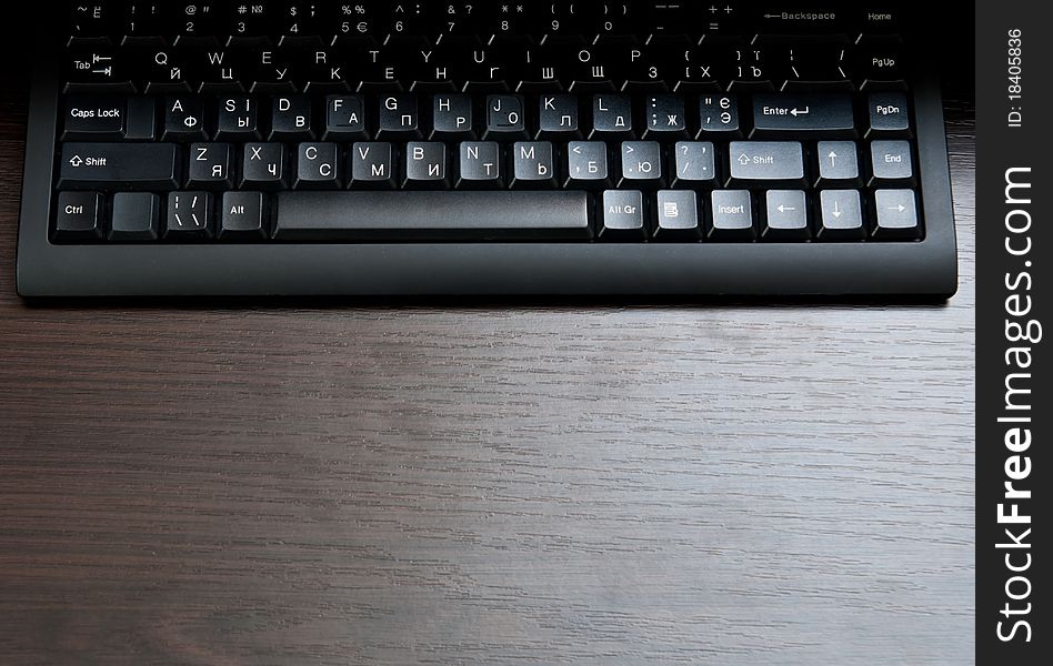 Single black keyboard on dark wood desk