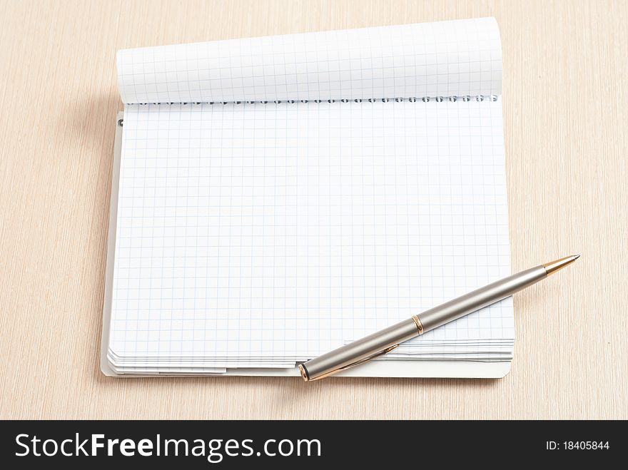 Blank spiral note pad with silver pen on wood. Blank spiral note pad with silver pen on wood