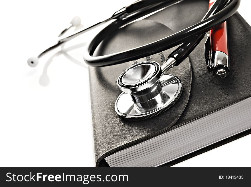 Close up macro of a black diary with red pen and a medical stethoscope on a white background with space for text. Close up macro of a black diary with red pen and a medical stethoscope on a white background with space for text
