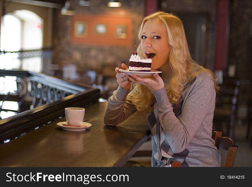 The charming girl drinks coffee with a cake in cafe