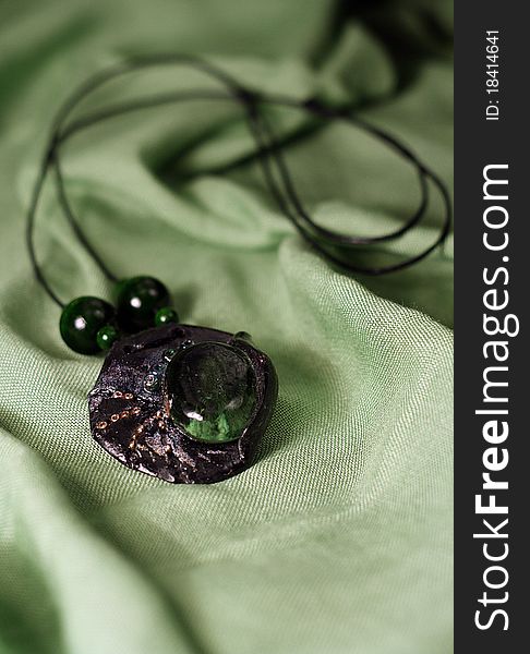 A green handmade pendant laying on a green satin scarf. A green handmade pendant laying on a green satin scarf