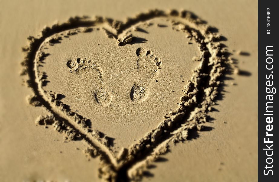 Some foot prints inside a heart drawn in the sand of a beach. Some foot prints inside a heart drawn in the sand of a beach
