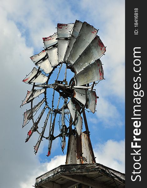 Metal windmill against blue sky with clouds.