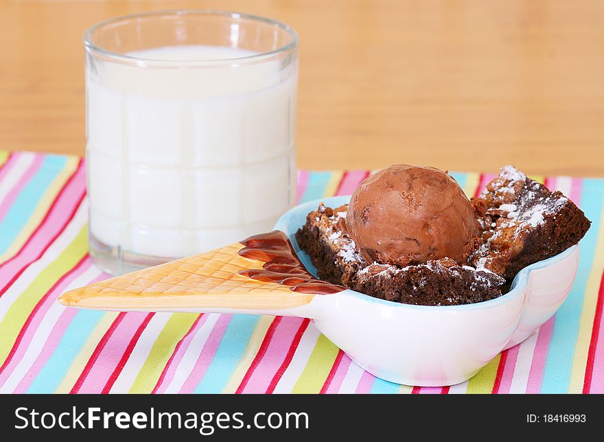 Brownie al a mode with chocolate ice cream and chocolate caramel brownies in a cute little ice cream brown with a glass of milk in the background on a striped place mat