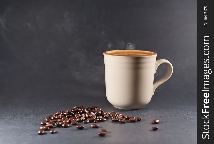 A steaming cup of coffee and coffee beans against a black background. A steaming cup of coffee and coffee beans against a black background