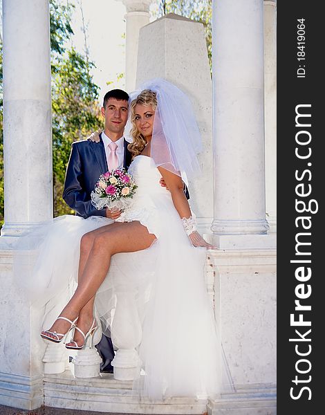 The bride and the groom in a marble arbor with columns