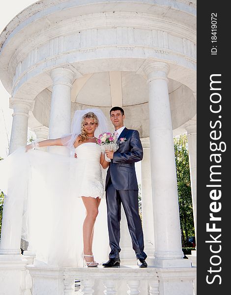 The bride and the groom in a marble arbor with columns