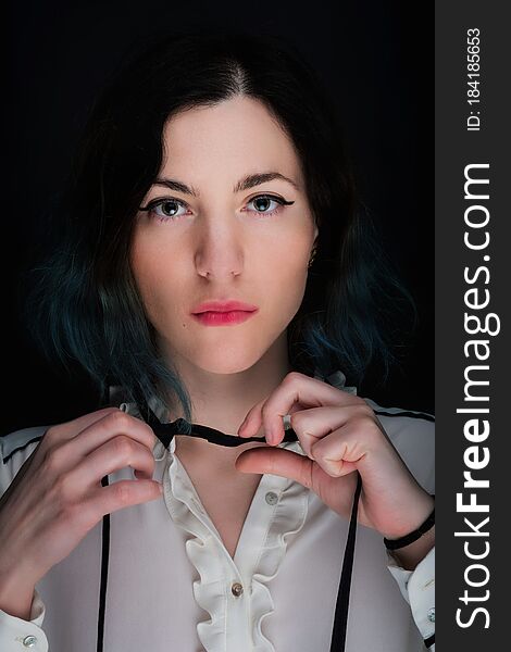Portrait of a young caucasian woman with serious face expression and black and blue gradient colored hair. Dark background, white blouse. Portrait of a young caucasian woman with serious face expression and black and blue gradient colored hair. Dark background, white blouse