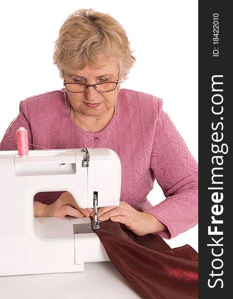 The elderly woman sews on the sewing machine on white