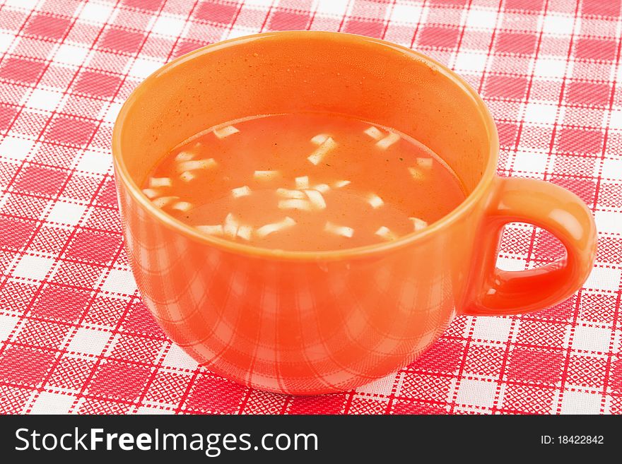 Orange bowl of tomatoes soup on red and white table cloth