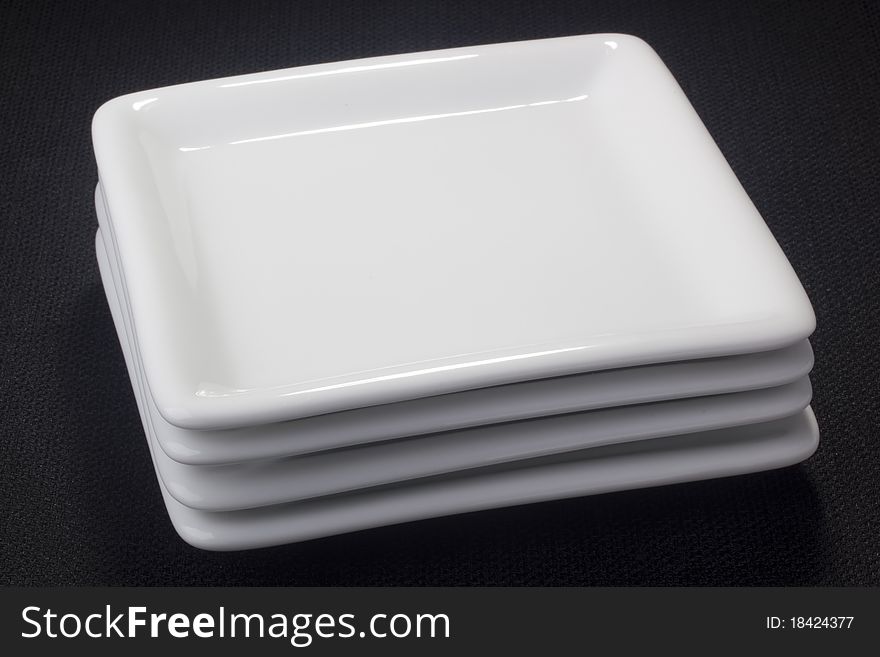White square ceramic plates for dessert dishes on a black background. White square ceramic plates for dessert dishes on a black background.