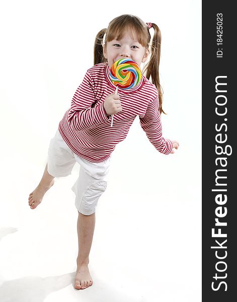 Dancing little girl eatis a lollipop isolated on white