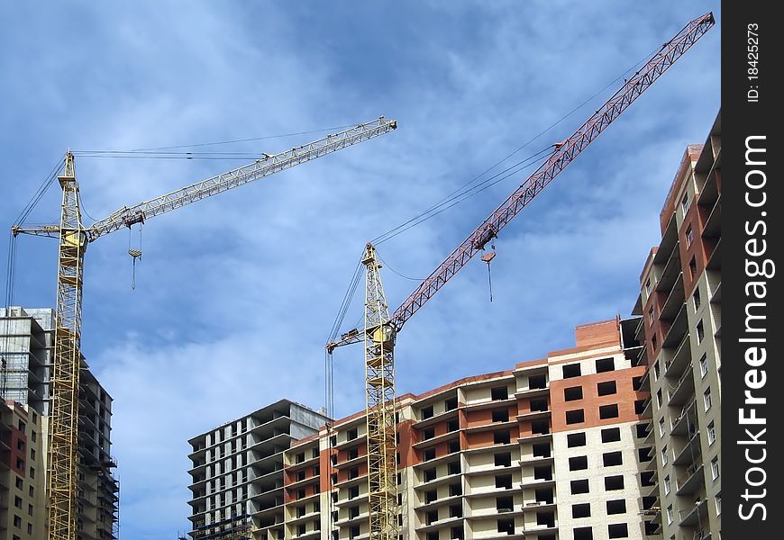 Under construction apartment house and two lifting cranes against a background of blue sky. Under construction apartment house and two lifting cranes against a background of blue sky