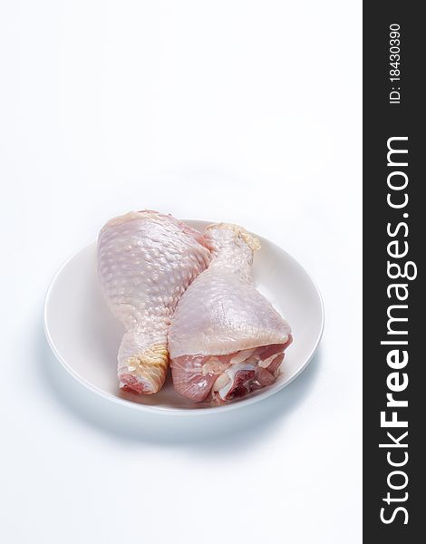 Two raw chicken legs on a plate on a white background