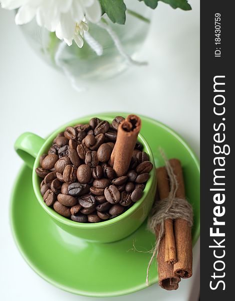 Coffee beans in a green cup and cinnamon sticks