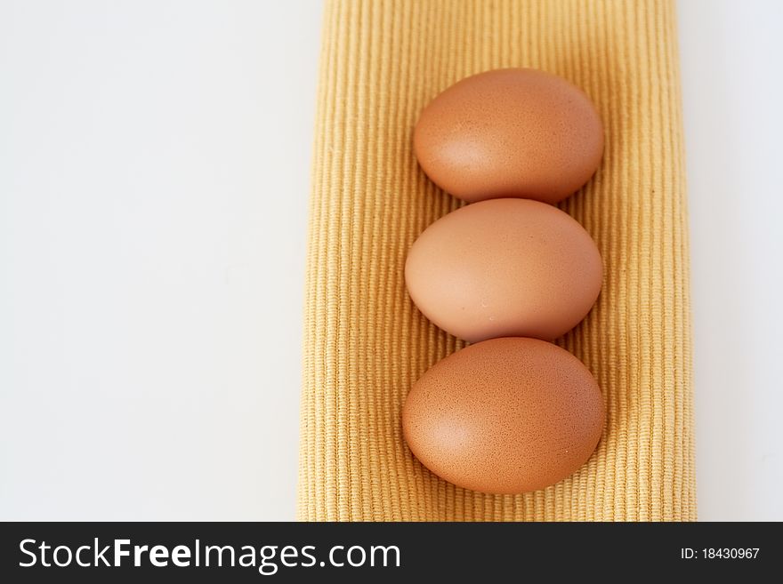 Three light brown eggs for breakfast are on a yellow towel. Three light brown eggs for breakfast are on a yellow towel