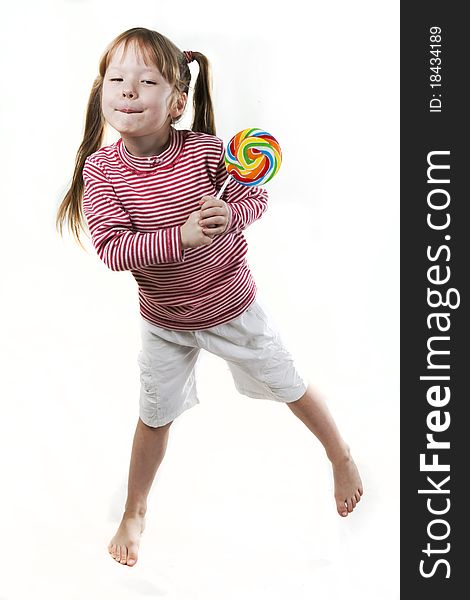 Dancing little girl eats a lollipop isolated on white