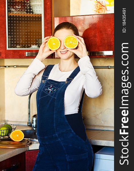 Smiling beautiful pregnant woman at kitchen with orange