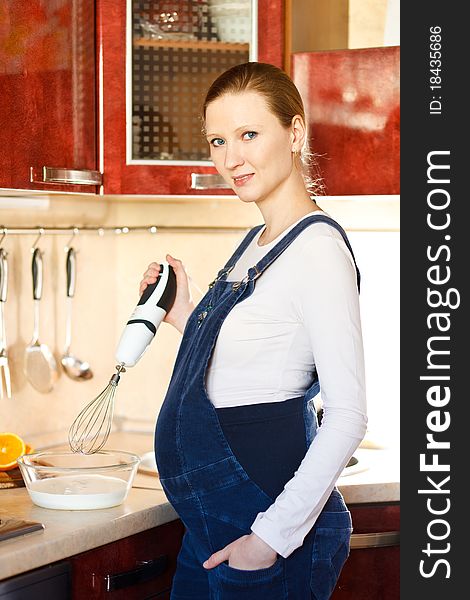 Young pregnant woman in kitchen making a food and smiling