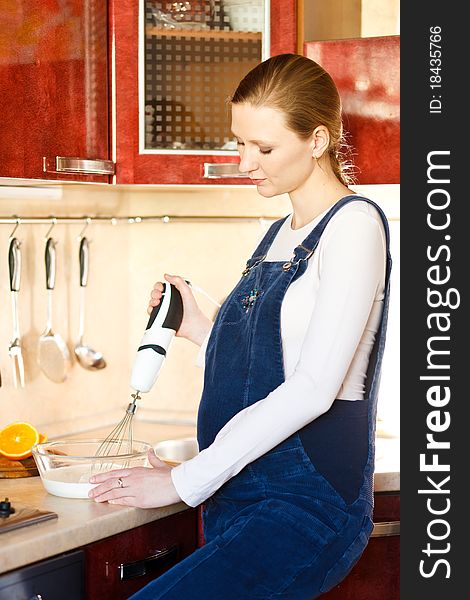Young pregnant woman in kitchen making a food