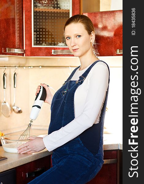 Young pregnant woman in kitchen making a food