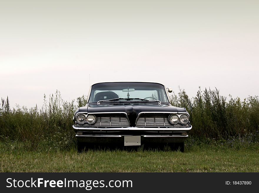 A black american 1960s car parked in a field. A black american 1960s car parked in a field