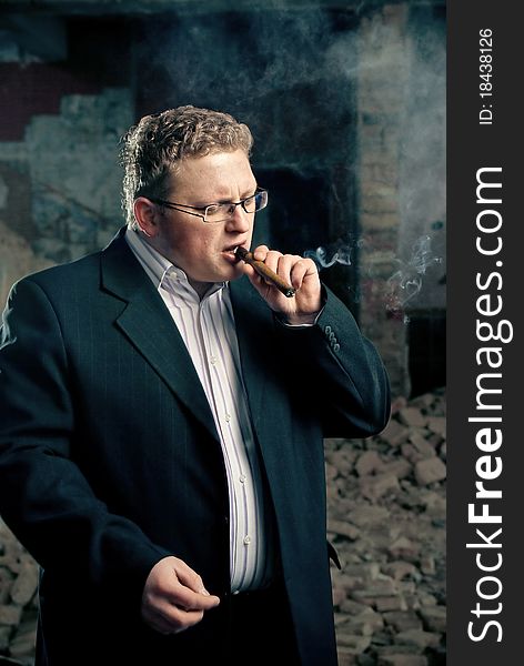 Man in black suite smoking cigar on abandoned factory background. Man in black suite smoking cigar on abandoned factory background