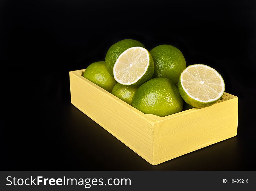Fresh green limes in a wooden box across black. Fresh green limes in a wooden box across black