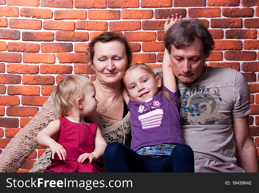 Happy seniors couple with grandchildren against brick wall