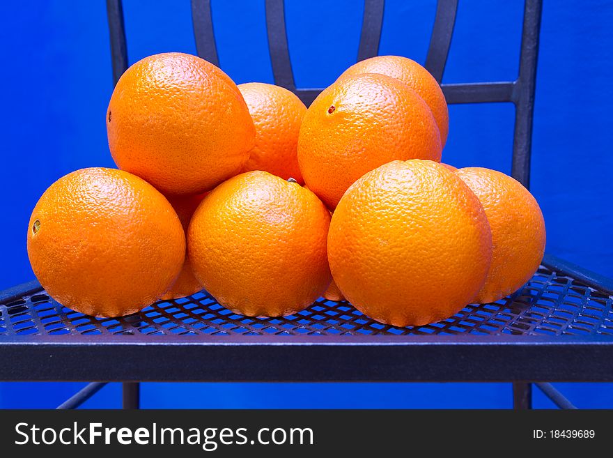Fresh Oranges on an iron chair in front of a blue wall. Fresh Oranges on an iron chair in front of a blue wall
