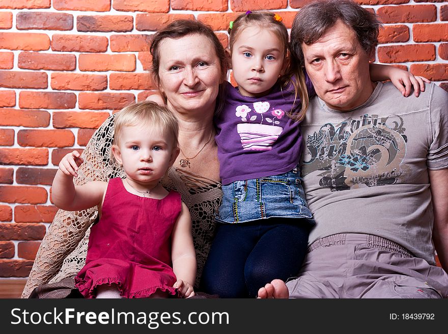 Happy seniors couple with grandchildren against brick wall