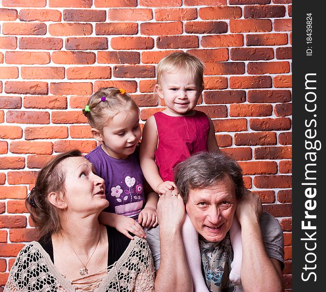 Happy seniors couple with grandchildren against brick wall