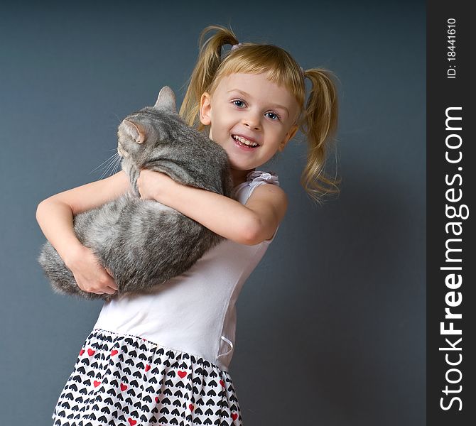 A girl with blond hair is holding a cat and laughs. A girl with blond hair is holding a cat and laughs