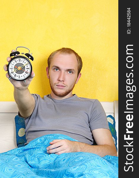 Man lying in bed and showing alarm clock