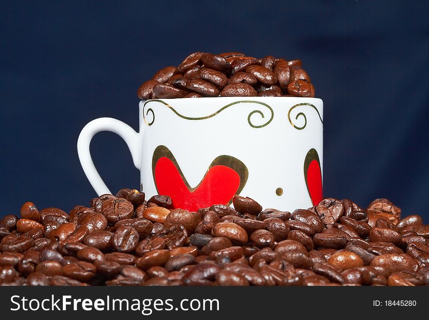 White cup with hearts stands sprinkle on the table beans roasted coffee. White cup with hearts stands sprinkle on the table beans roasted coffee.