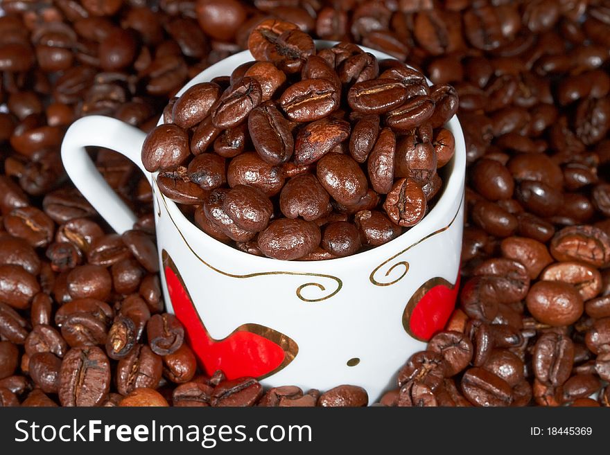 White cup with hearts stands sprinkle on the table beans roasted coffee. White cup with hearts stands sprinkle on the table beans roasted coffee.