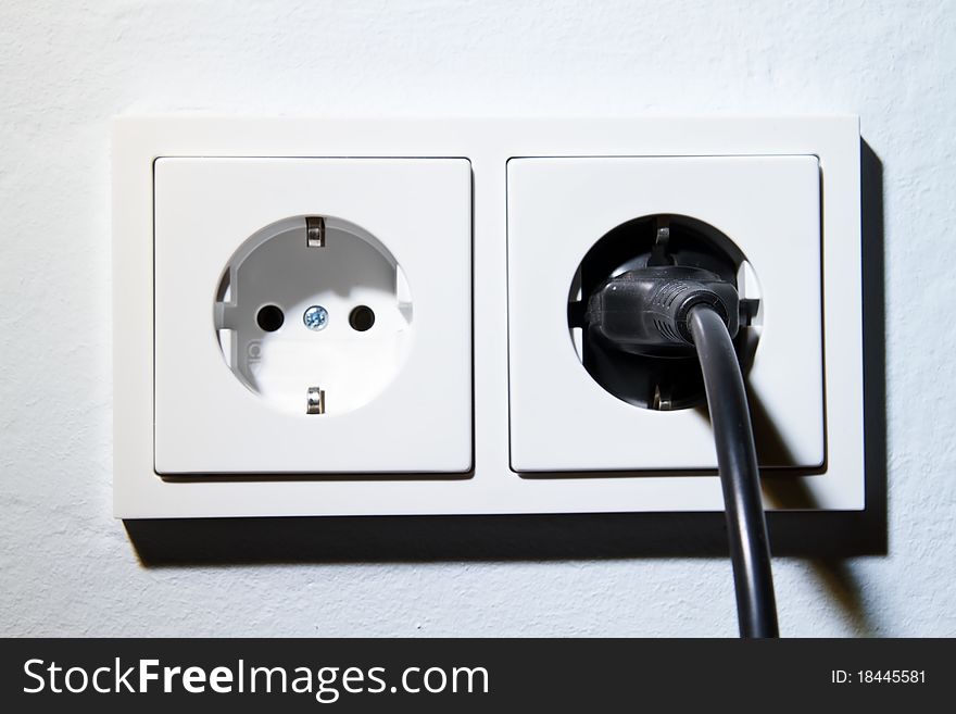 Electrical outlet with plug on white painted wall