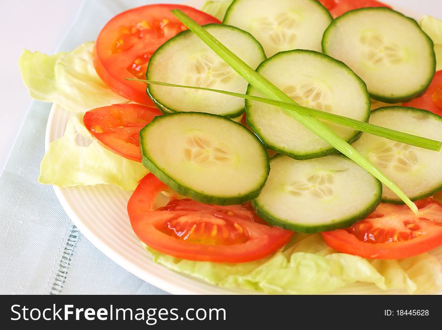 Fresh salad with cucumber, tomato and lettuce with chives garnish on white plate. Fresh salad with cucumber, tomato and lettuce with chives garnish on white plate