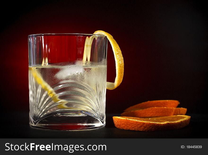 Cold vodka in a glass, with decor oranges and lemon, in black red background, part of art beverage background. Cold vodka in a glass, with decor oranges and lemon, in black red background, part of art beverage background