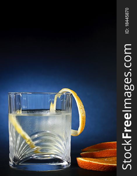 Cold vodka in a glass, with decor oranges and lemon, in black blue background, part of art beverage background. Cold vodka in a glass, with decor oranges and lemon, in black blue background, part of art beverage background