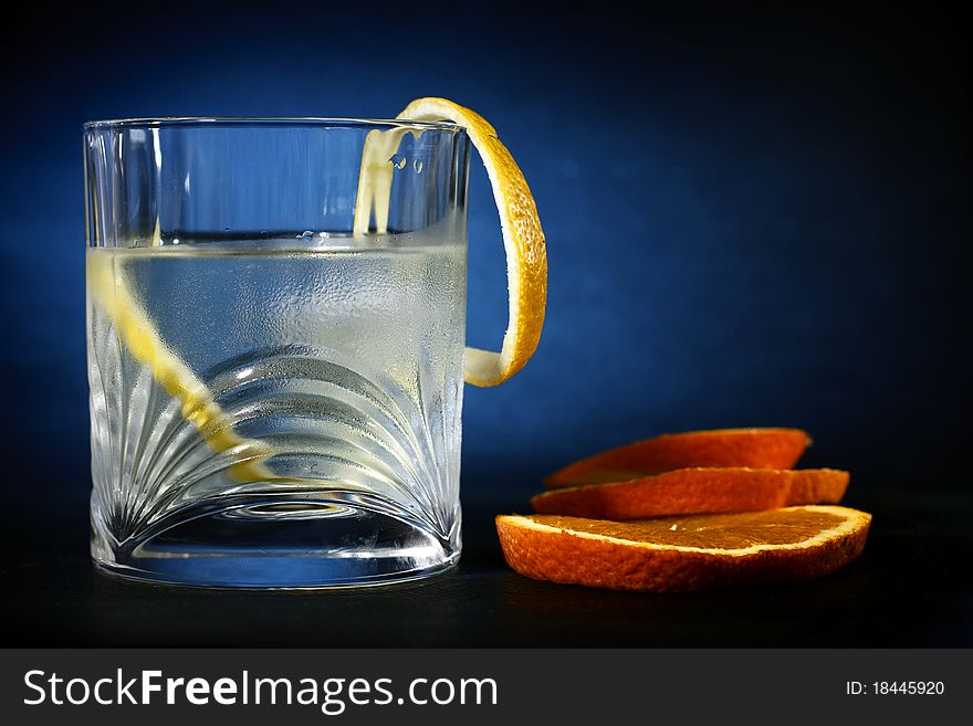 Cold vodka in a glass, with decor oranges and lemon, in black blue background, part of art beverage background. Cold vodka in a glass, with decor oranges and lemon, in black blue background, part of art beverage background