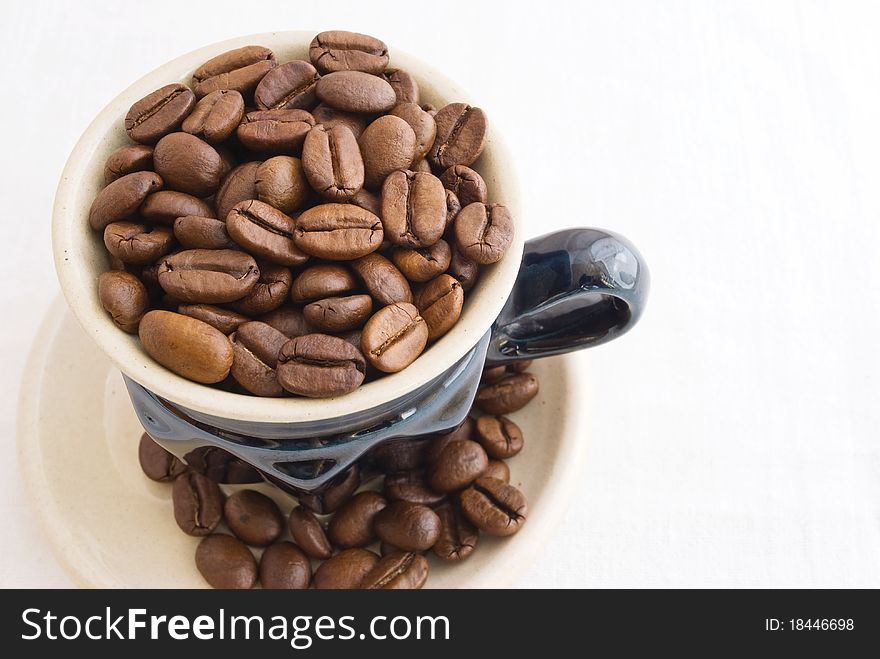 Grain, black coffee sprinkled in small coffee cup with saucer, taken pictures close-up several overhand, on background light fabrics. Grain, black coffee sprinkled in small coffee cup with saucer, taken pictures close-up several overhand, on background light fabrics.