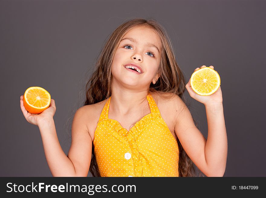 Cute young girl with oranges on gray background