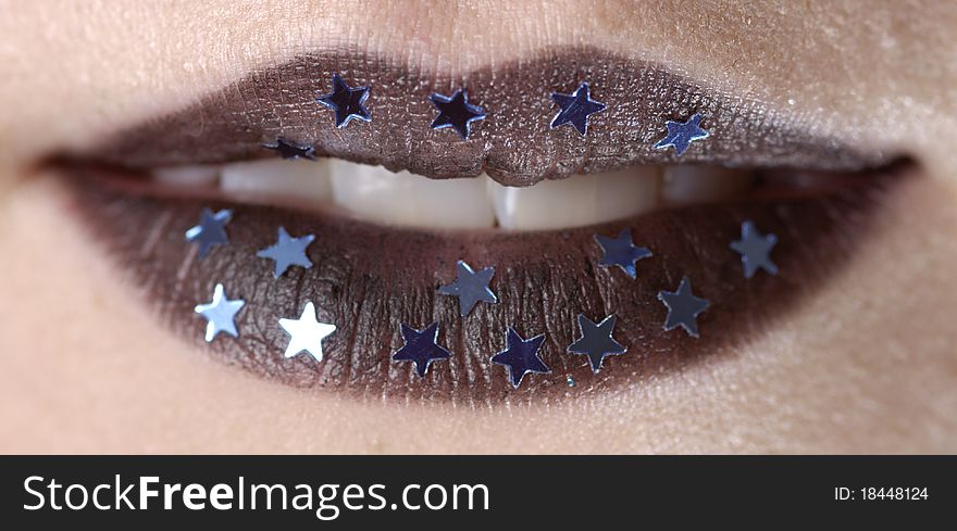 Close-up shot of a woman's open mouth with black lipstick and stars stuck to her lips.