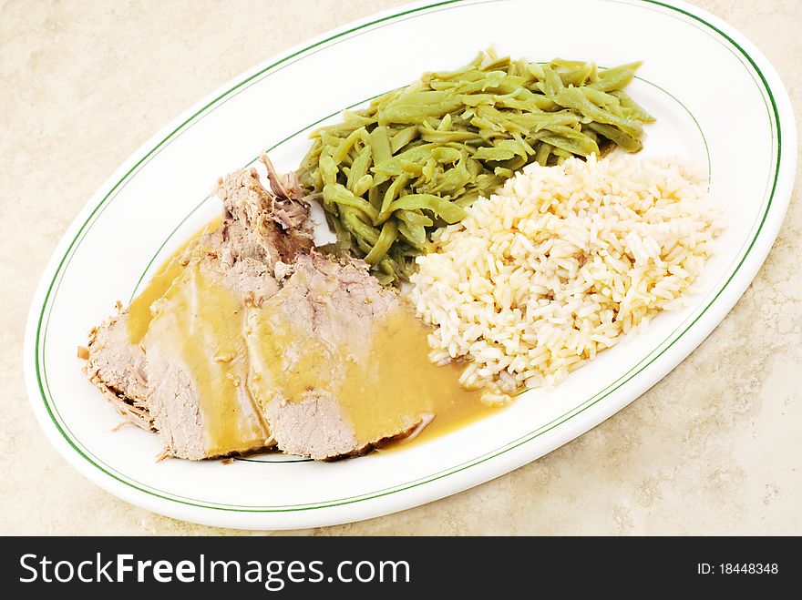 Sliced roast beef with gravy, brown rice and french style green beans on a dinner plate. Sliced roast beef with gravy, brown rice and french style green beans on a dinner plate