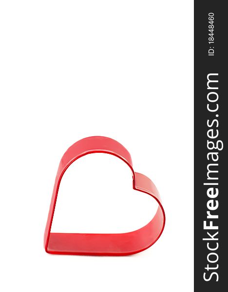 A metal red heart cookie cutter on a vertical white background with copy space. A metal red heart cookie cutter on a vertical white background with copy space