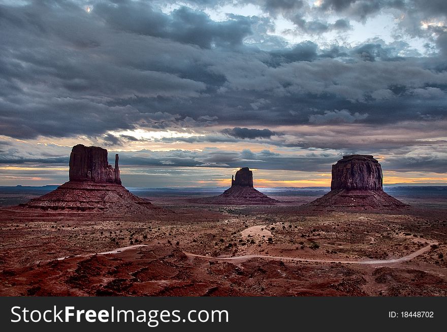Monument valley three buttes cloudy sunrise with road in the foreground and dark clouds. Monument valley three buttes cloudy sunrise with road in the foreground and dark clouds