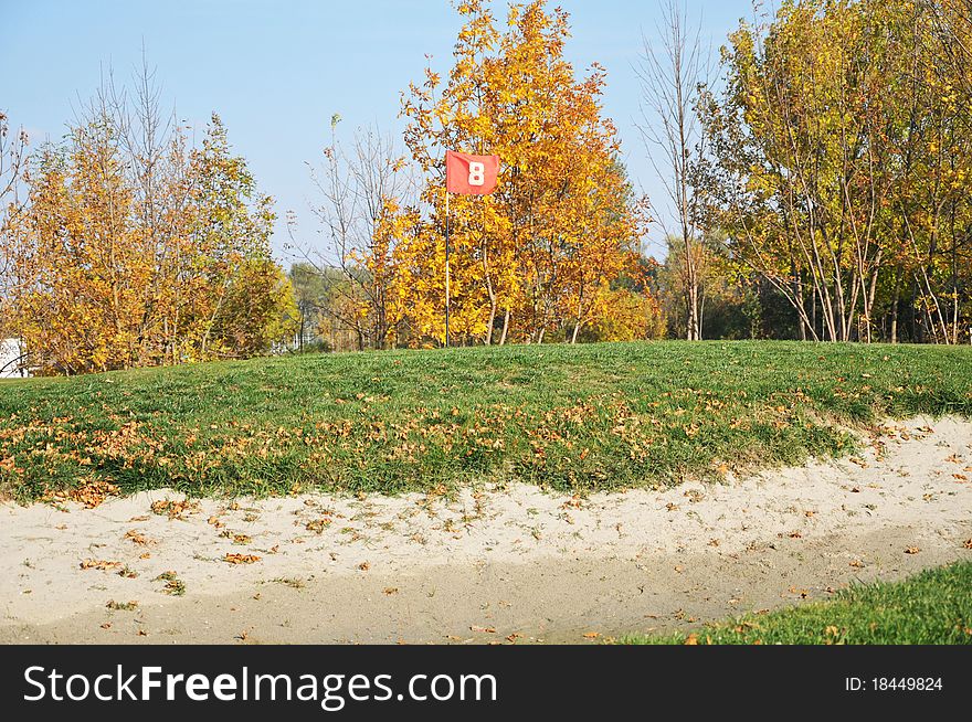 Golf field.flag, sand and trees with autumn colors